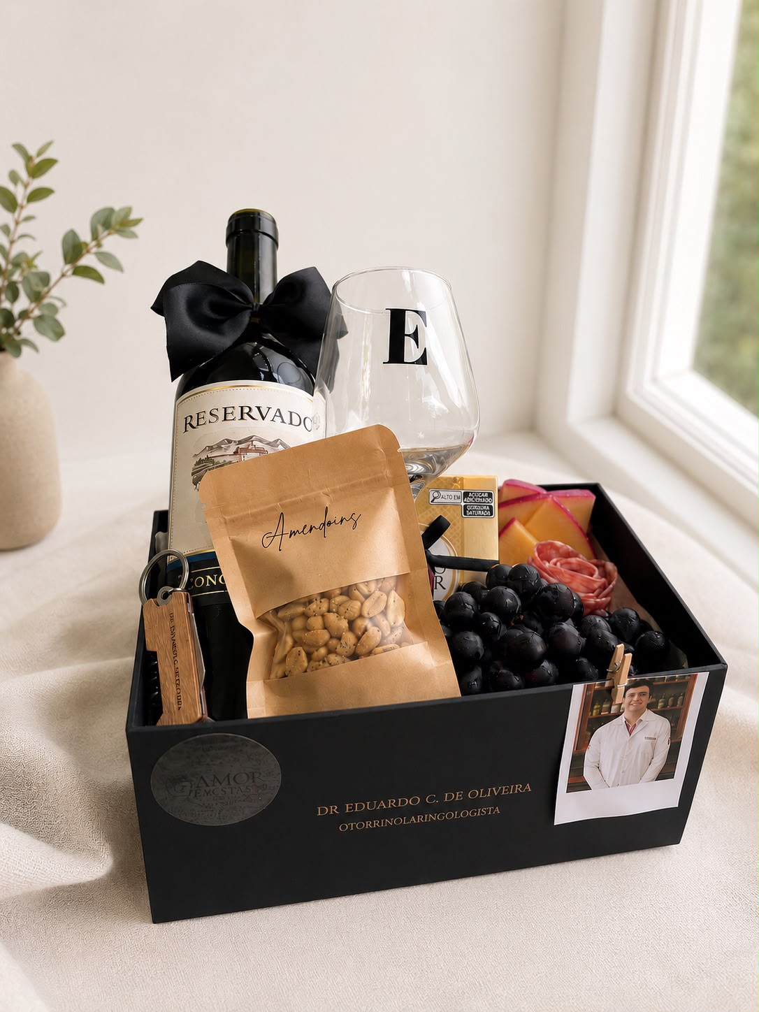 Queijos, Salame formato rosa, 1 vinho reservado, 01 taça personalizada, 01 sachê de amendoim, 01 Ferreiro Rocher, 01 poloroide, uvas, 01 abridor personalizado. 