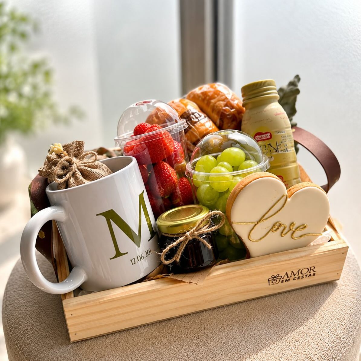Cesta café - 1 Massa doce , 1 Massa salgada, 01 pote c/ morangos , 01 pote c/ uvas , 01 Bebida Lactea, 01 Pilha de torradas , 01 Biscoito decorado, 01 Caneca personalizada, 01 Sachê de biscoitinhos, 01 Cesta de madeira em courino. 